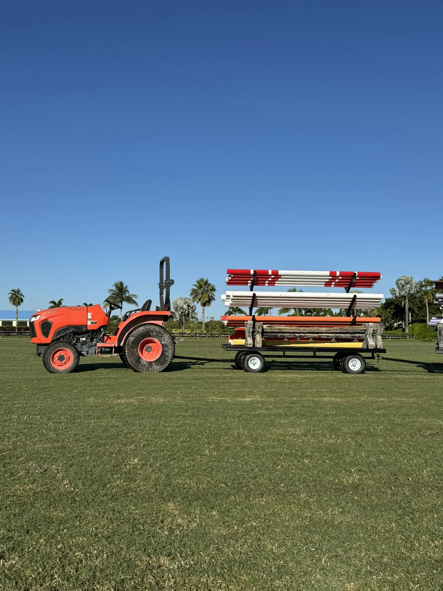 Kubota tractor pulling a wagon of red and white jump poles across the show field